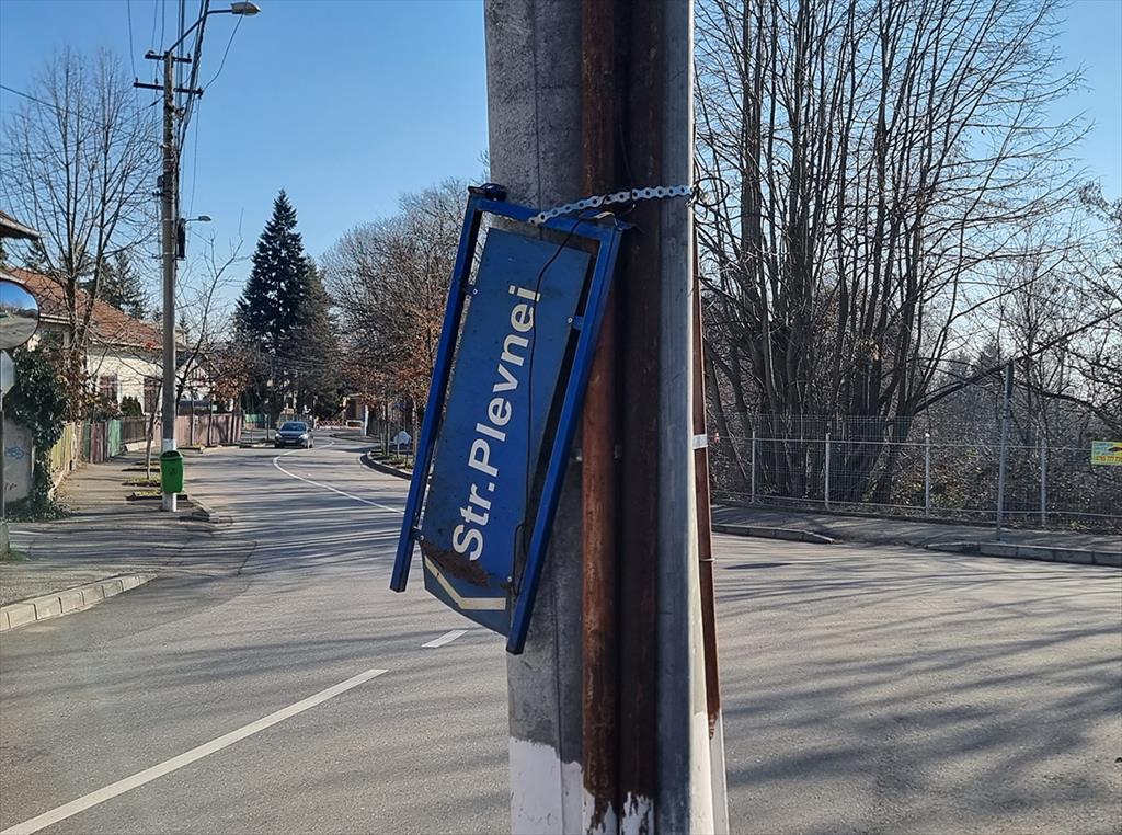 Синя табела Str. Plevnei, наклонена и закрепена с верига към стълб на кръстовище в Къмпина.