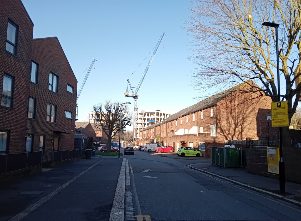 Plevna Crescent в South Tottenham, Лондон: тухлени жилищни сгради, паркирани автомобили и строителни кранове на заден план.